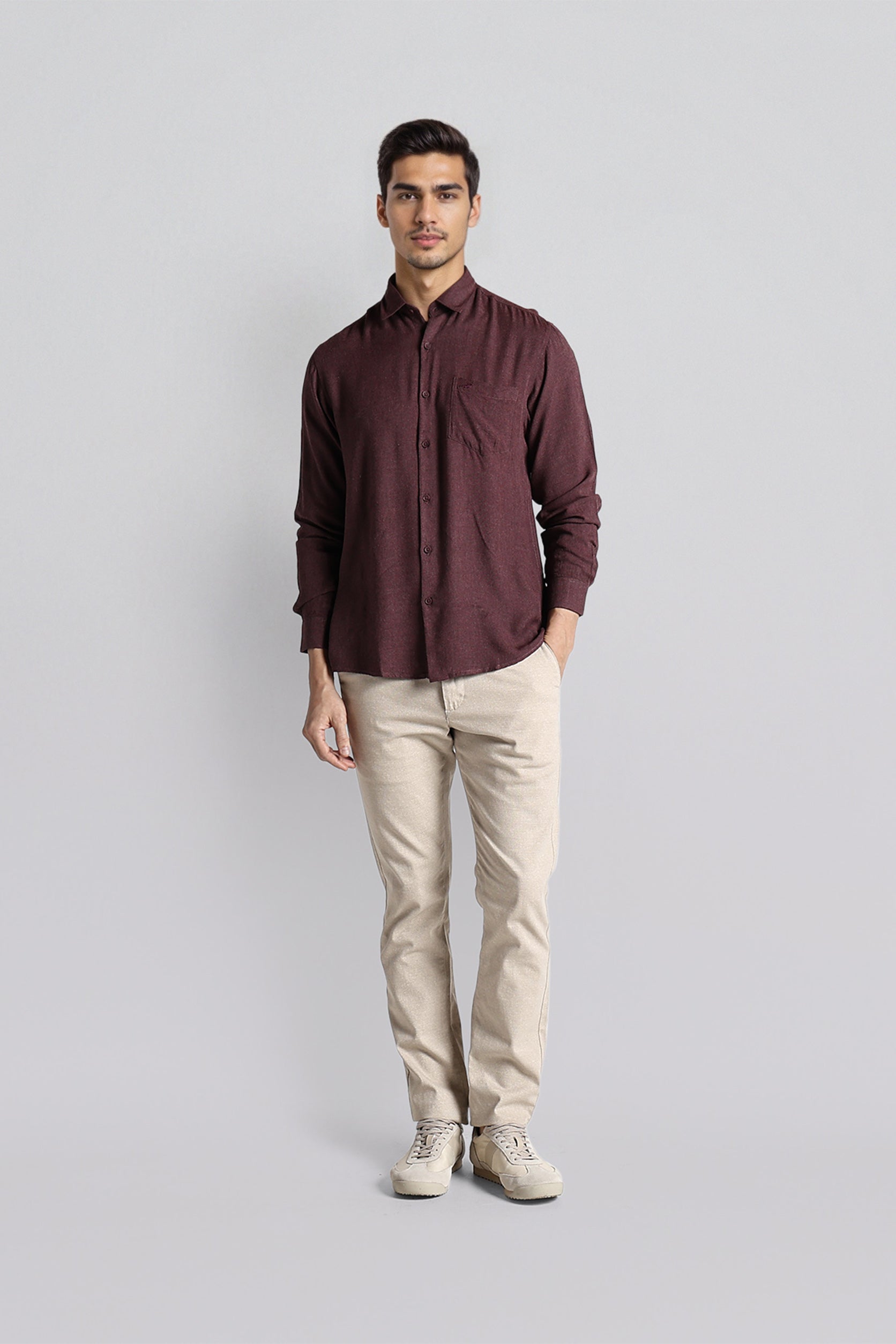 Man wearing a maroon shirt and beige pants on a light gray background