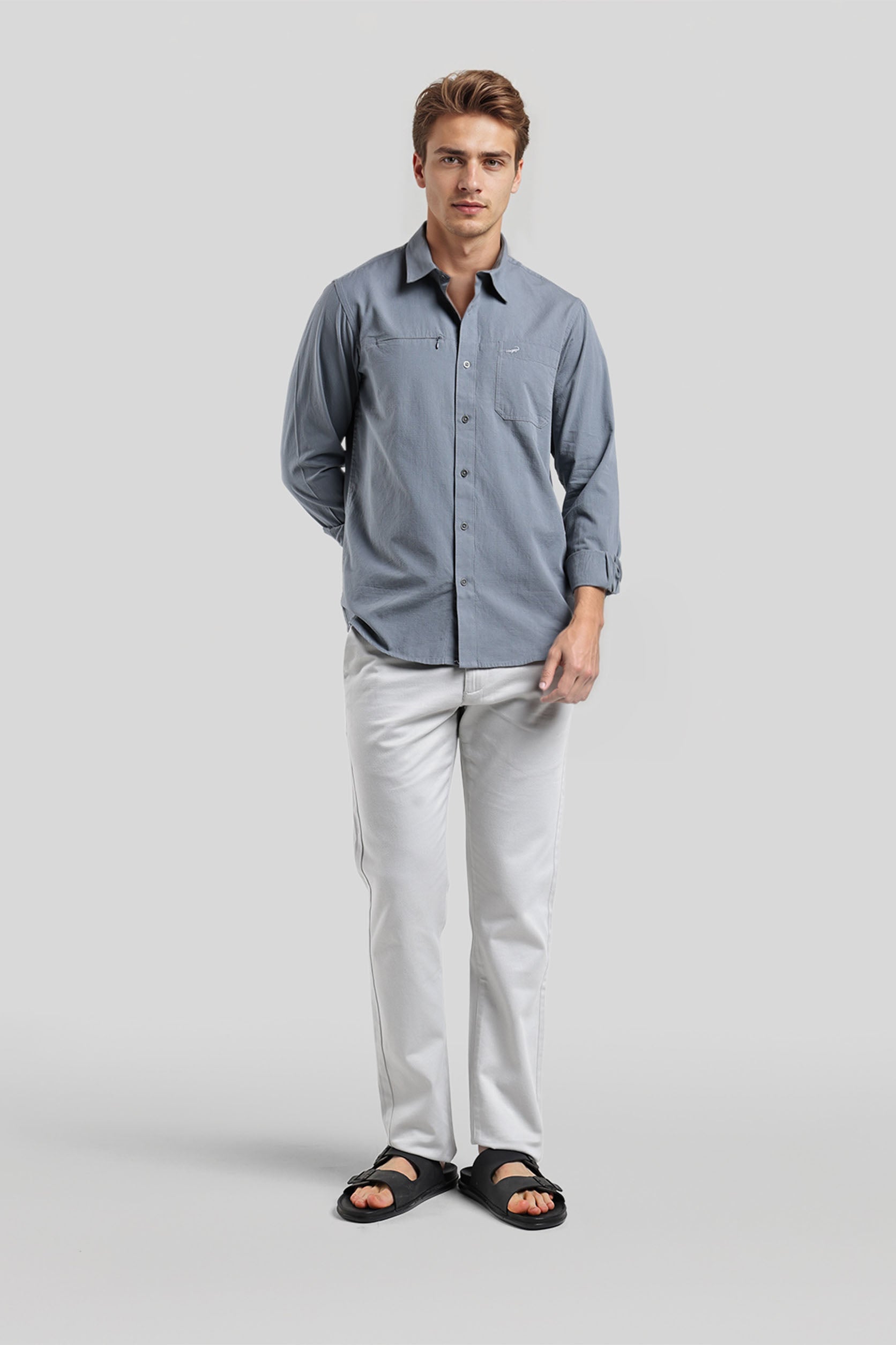 Man wearing a blue button-up shirt and light gray pants on a white background