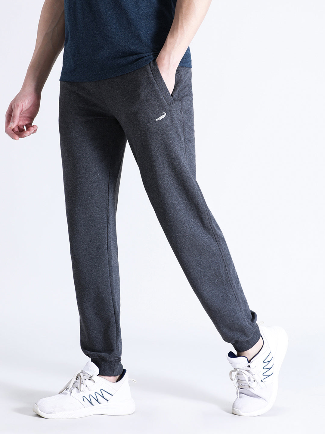 A person standing wearing charcoal grey classic fit joggers with a solid pattern, paired with a blue top and white sneakers.
