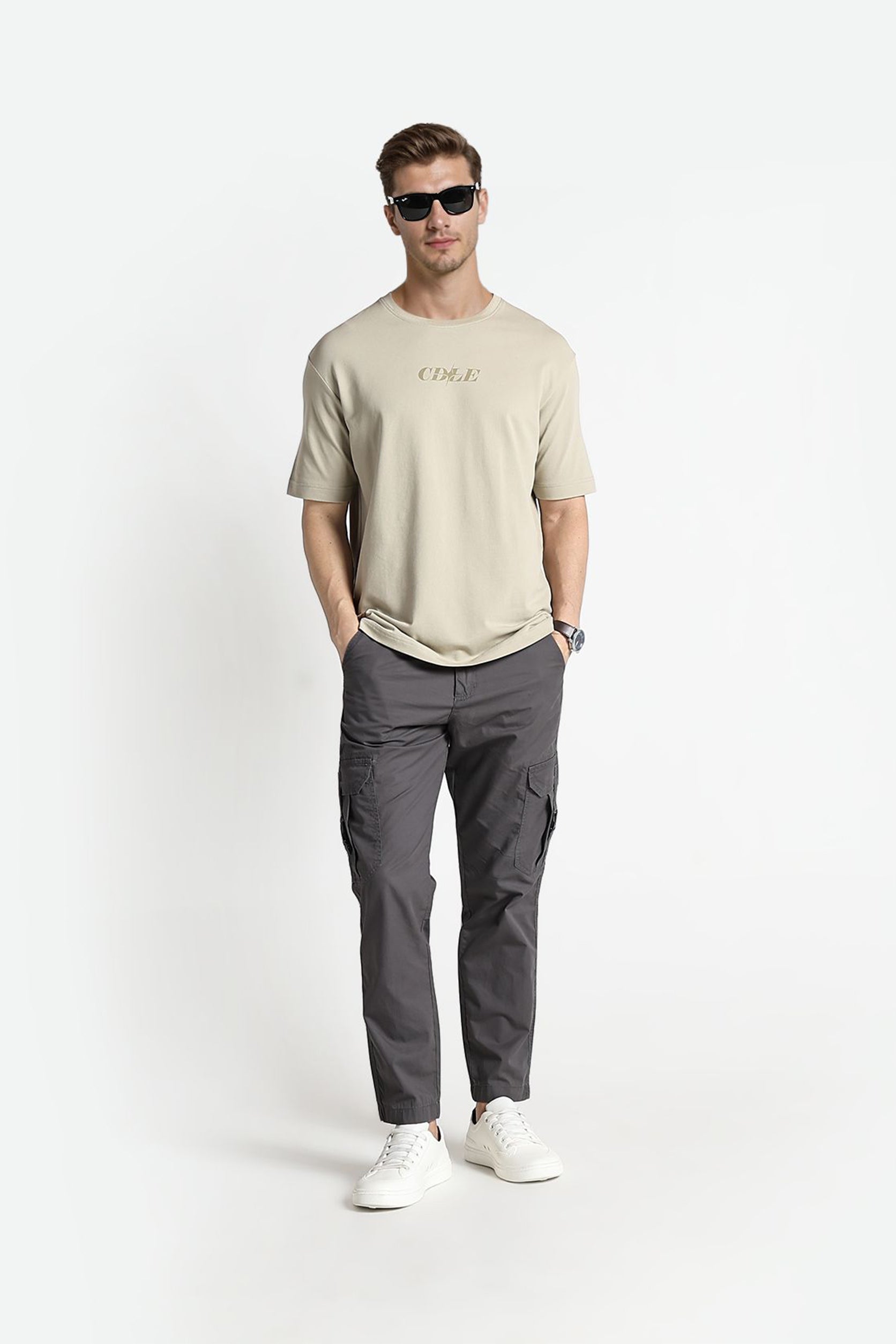 Man wearing a beige t-shirt and gray pants on a white background