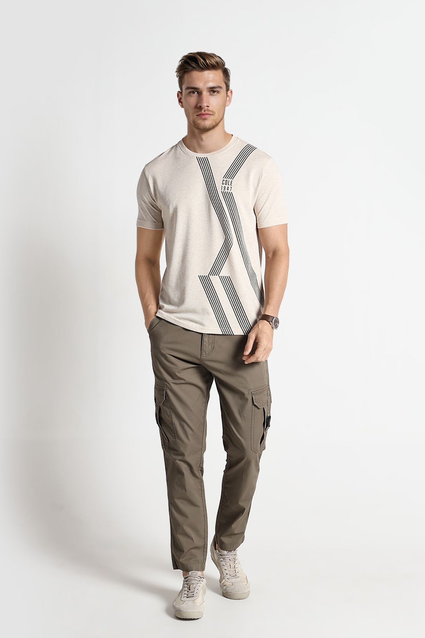 Man wearing a beige t-shirt with a geometric design and green cargo pants on a white background