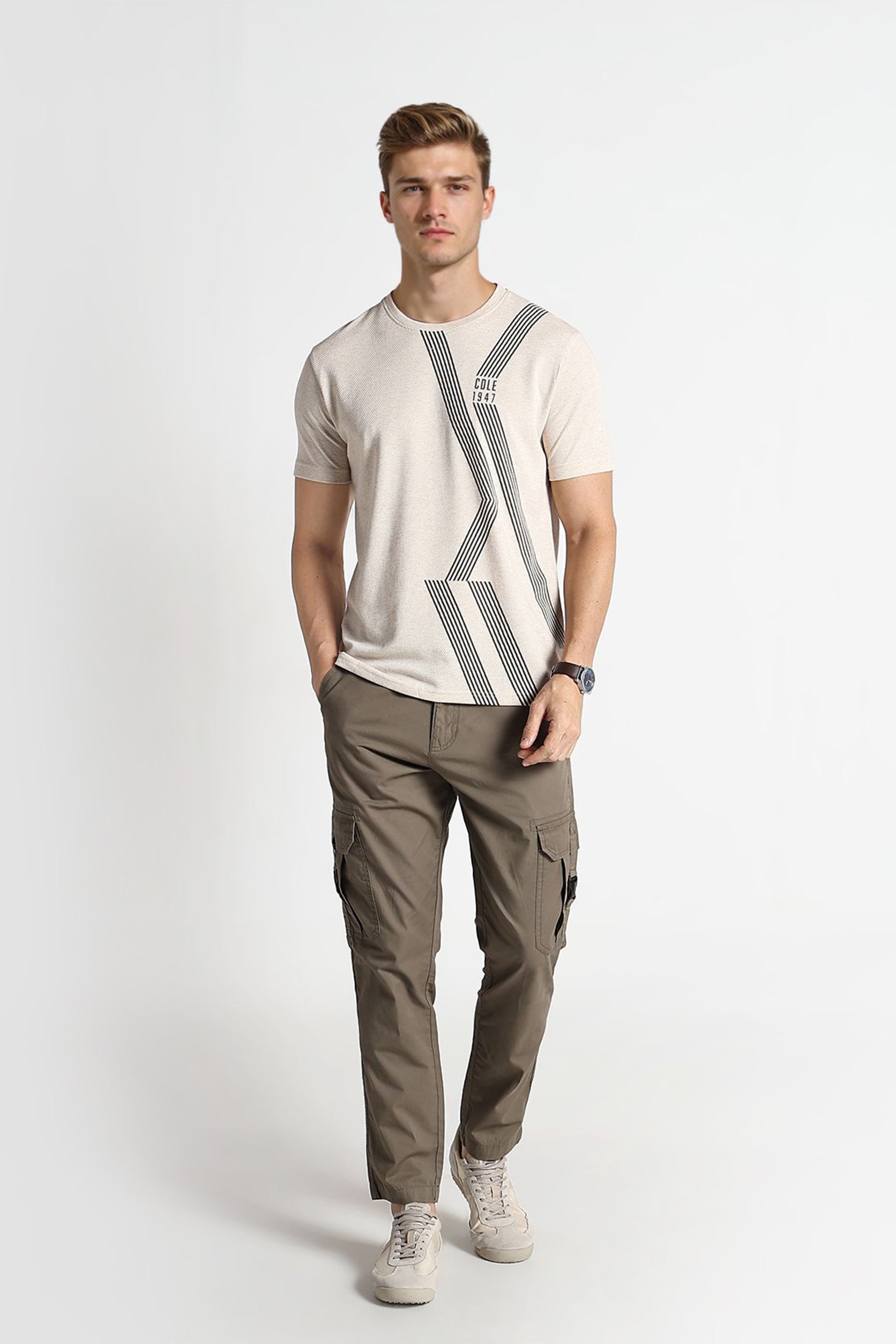 Man wearing a beige t-shirt with a graphic design and green cargo pants on a white background