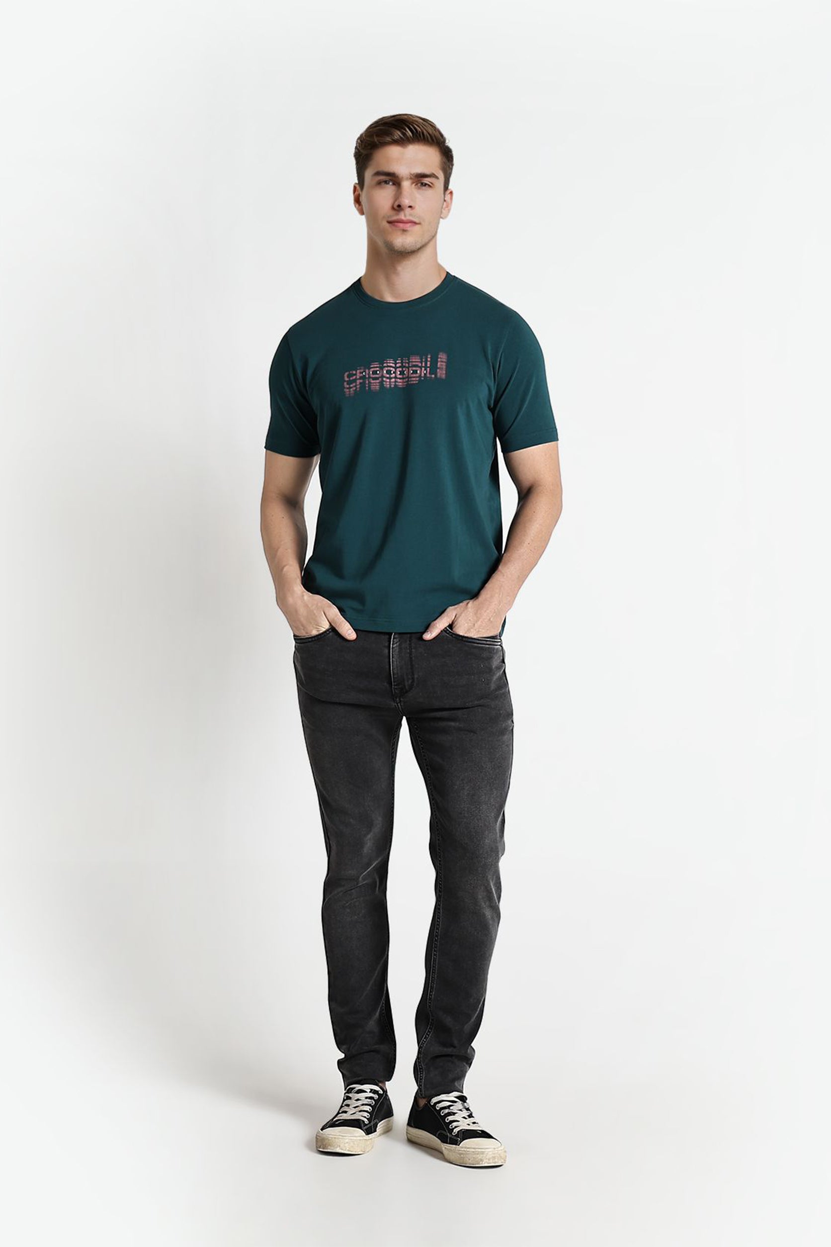 Man wearing a green t-shirt with text and dark jeans on a white background