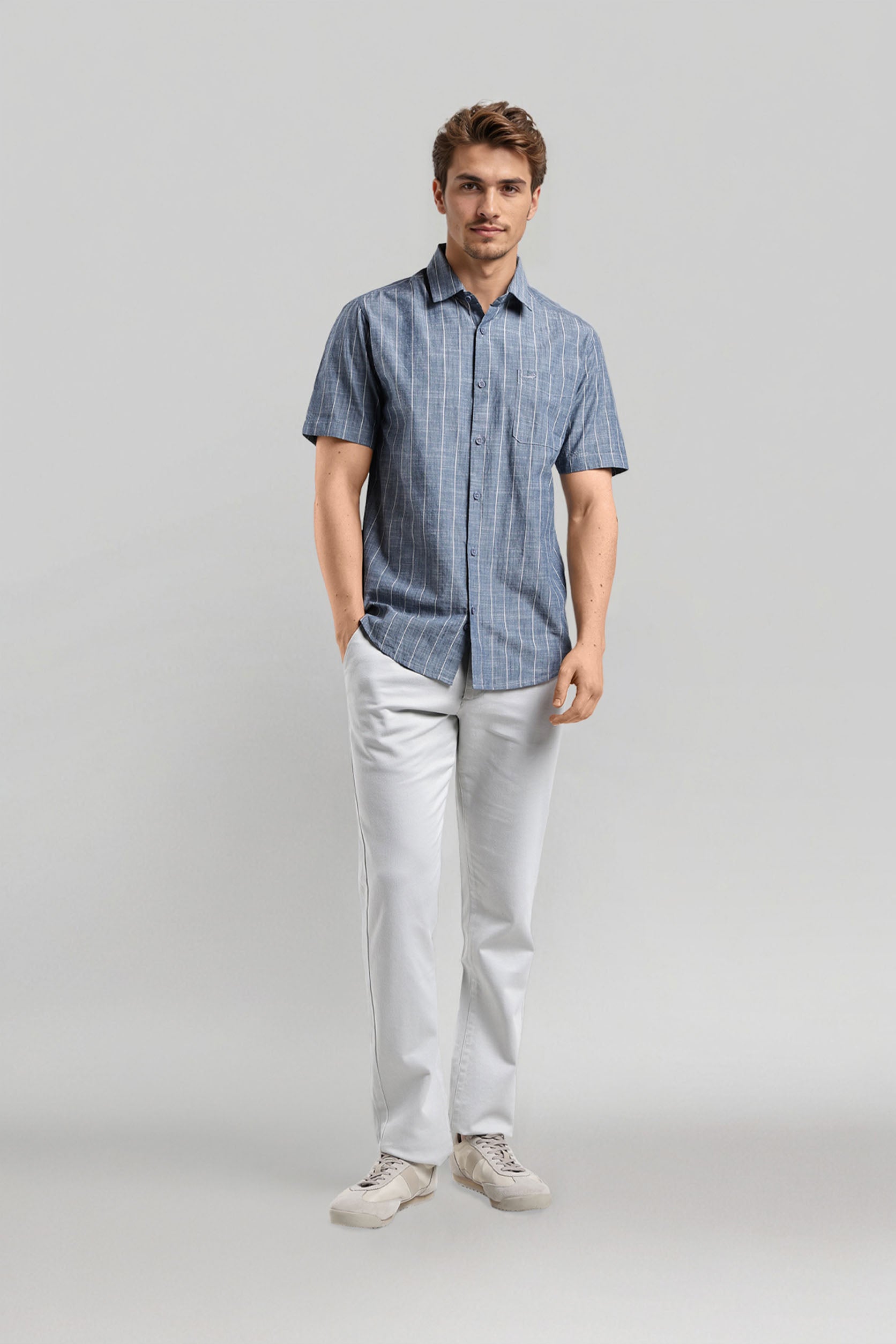 Man wearing a blue checkered shirt and white pants on a gray background