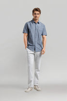 Man wearing a blue checkered shirt and white pants on a gray background