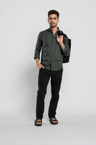 Man wearing a green shirt and black pants holding a black jacket against a white background