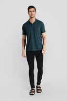 Man wearing a dark green polo shirt and black pants on a light gray background