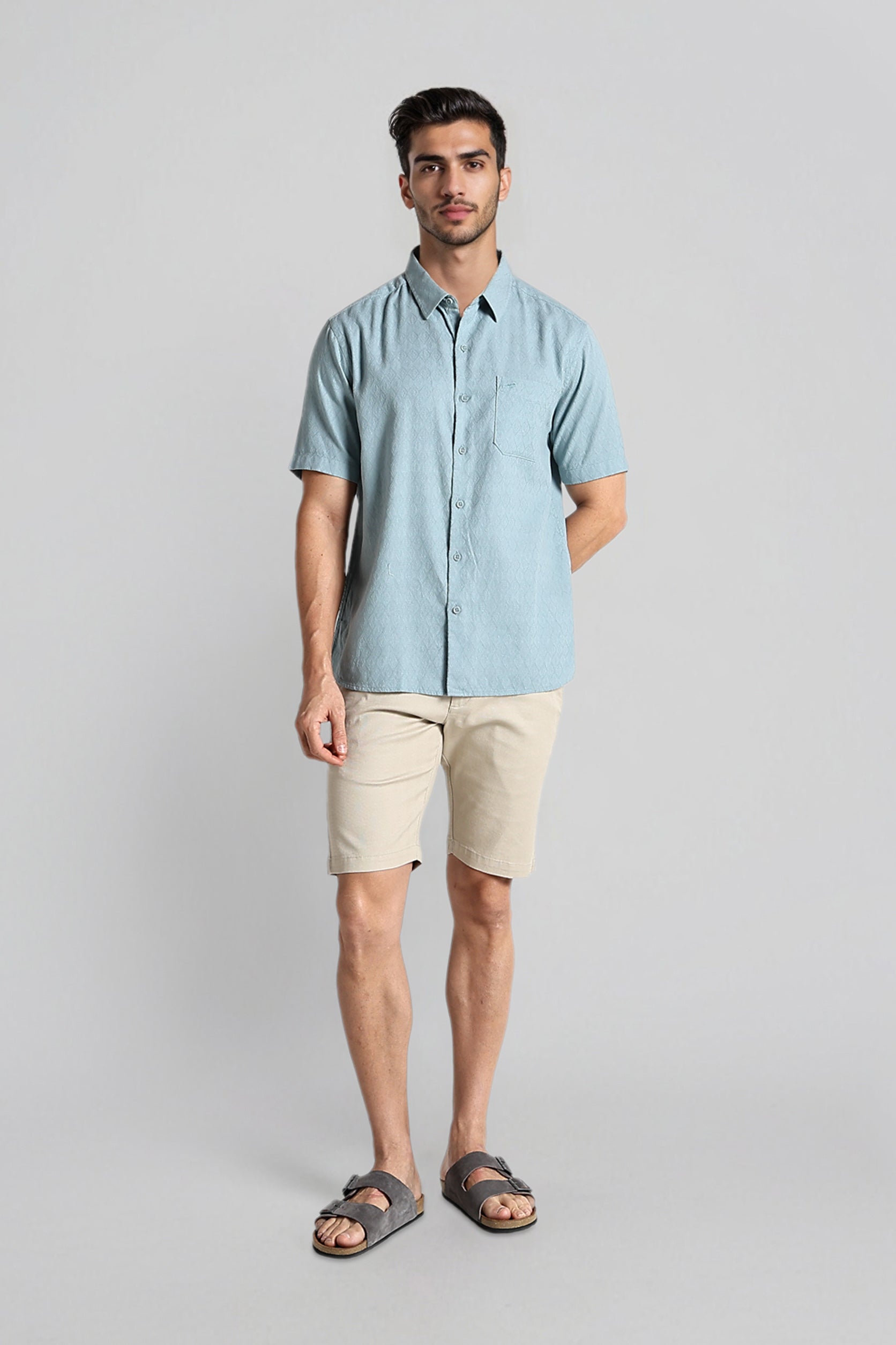 Man wearing a light blue shirt and beige shorts on a gray background