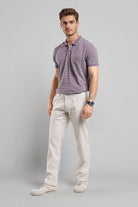 Man wearing a striped polo shirt and light-colored pants on a gray background