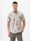A man wearing a short-sleeve button-up shirt with a beige and brown floral pattern, paired with gray trousers, standing against a plain white background.