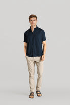 Man wearing a navy shirt and beige pants on a gray background