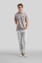 Man wearing a striped polo shirt and light-colored pants on a gray background