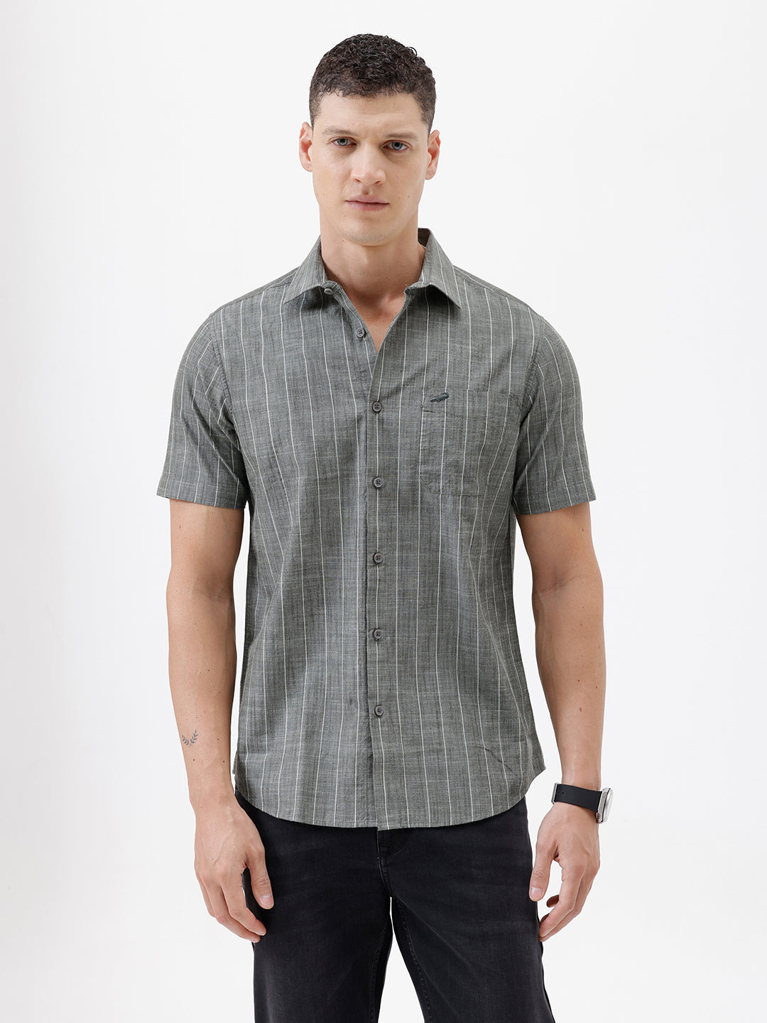 A man wearing a short-sleeve button-up shirt with a gray and white vertical stripe pattern, paired with black pants, standing against a plain white studio background.