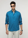 Man wearing a teal abstract print satin shirt with casual styling on a gray background