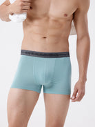 Man wearing teal boxer briefs with a gray waistband on a white background