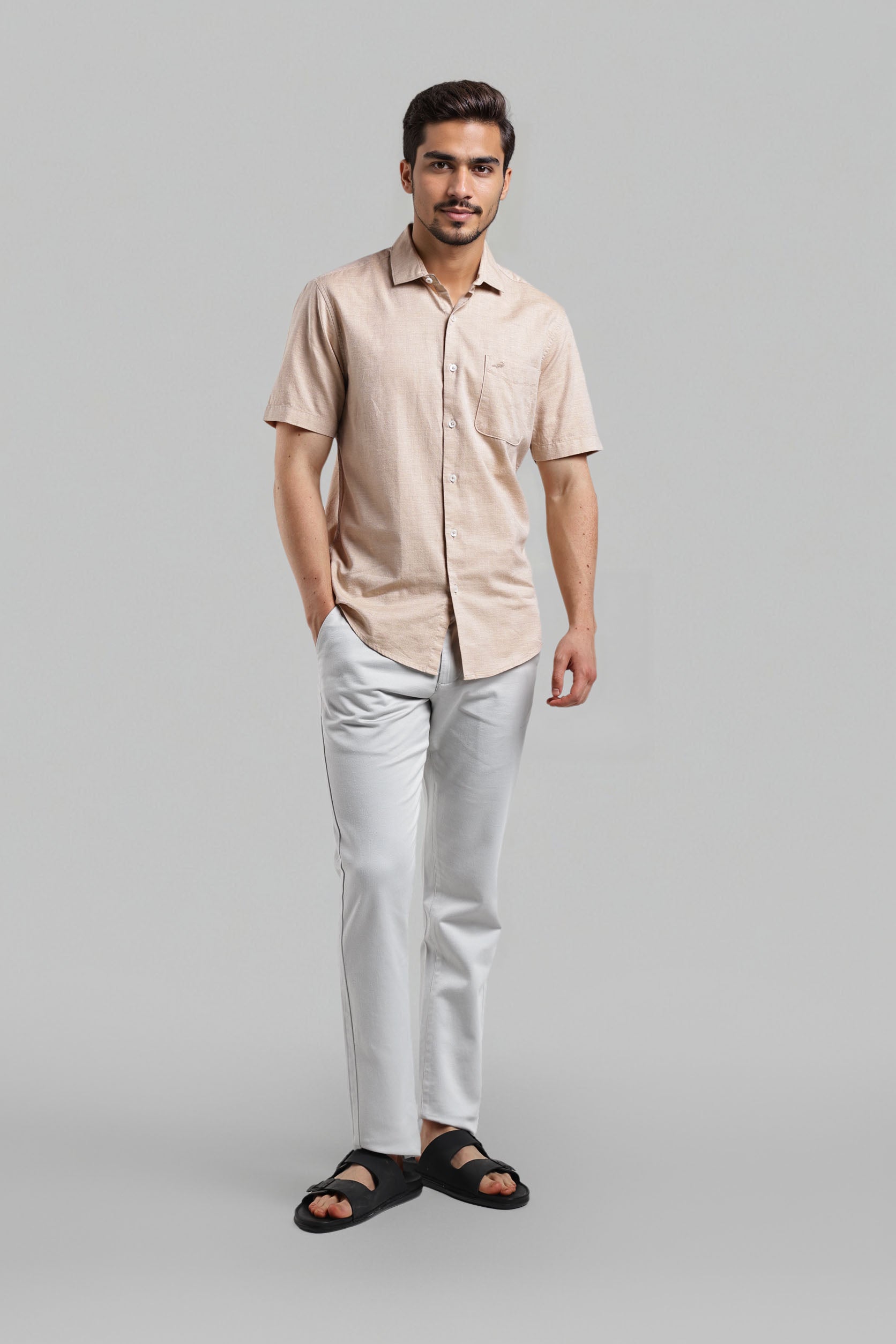 Man wearing a beige shirt and white pants on a gray background