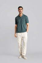 Man wearing a green polo shirt and white pants on a gray background