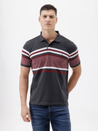 A man wearing a dark gray Lacoste polo shirt with horizontal red and white stripes across the chest and sleeves, paired with blue jeans, against a plain light gray background.