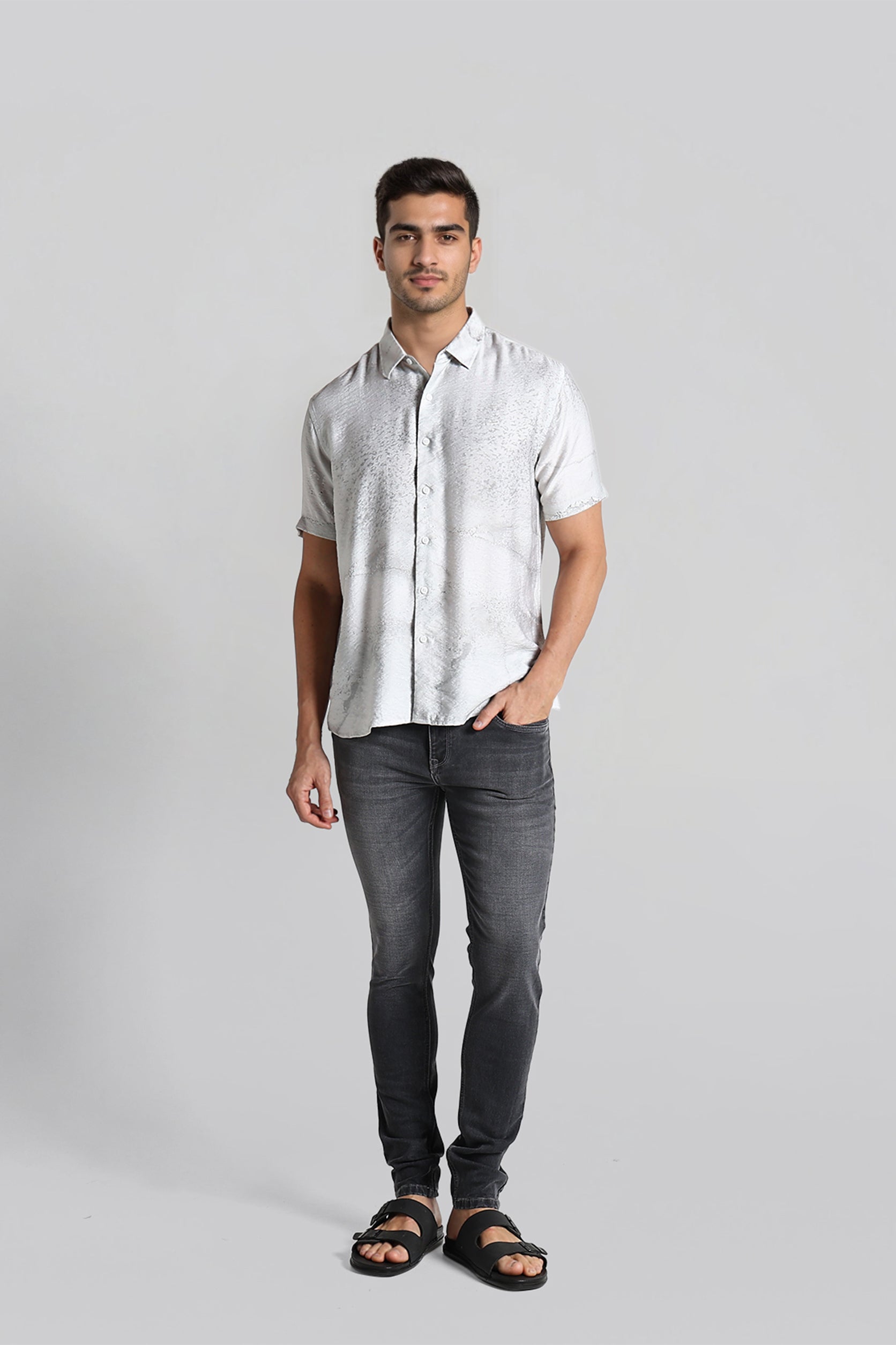 Man wearing a white shirt and dark jeans on a gray background