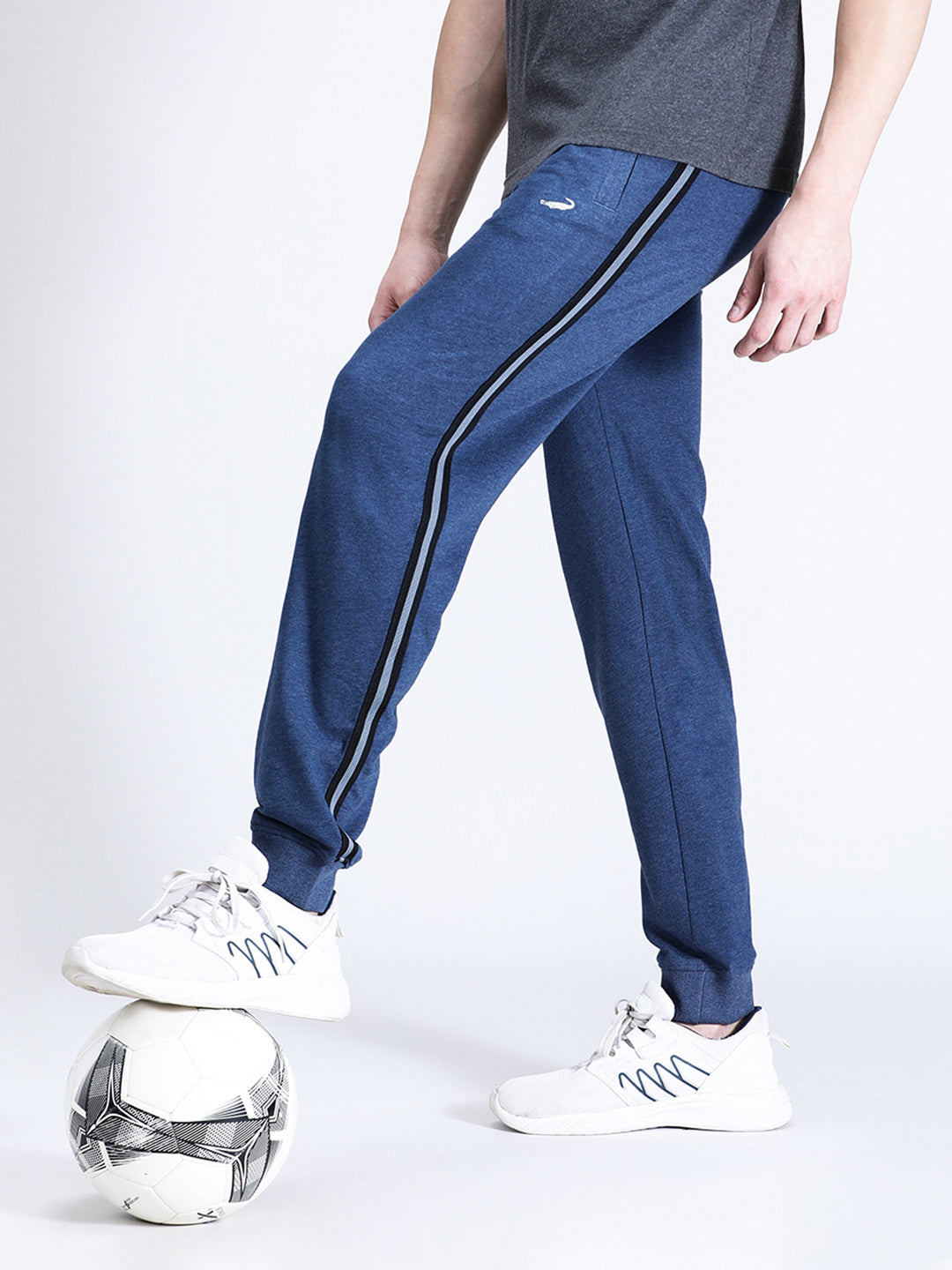 A person standing with one foot on a soccer ball, wearing blue melange solid classic fit joggers and white sneakers.