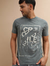 Man wearing a green dark forest green printed t shirt with casual styling on a gray background
