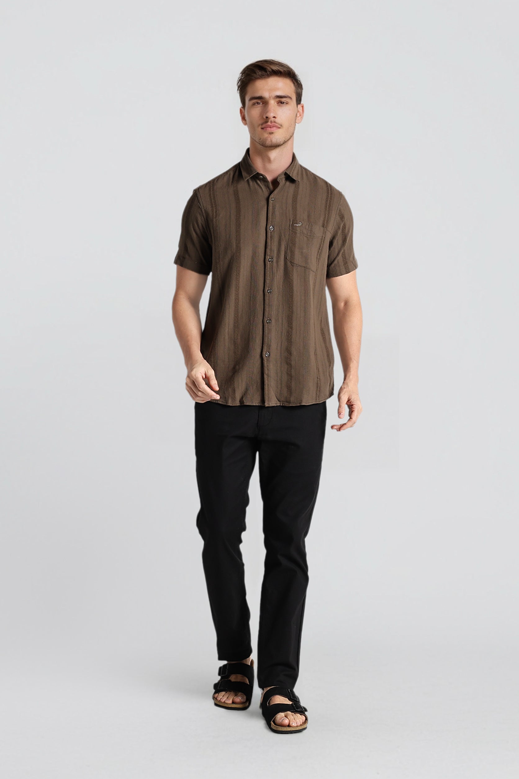 Man wearing a brown short-sleeve shirt and black pants on a light gray background