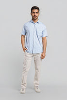 Man wearing a light blue shirt and beige pants on a gray background