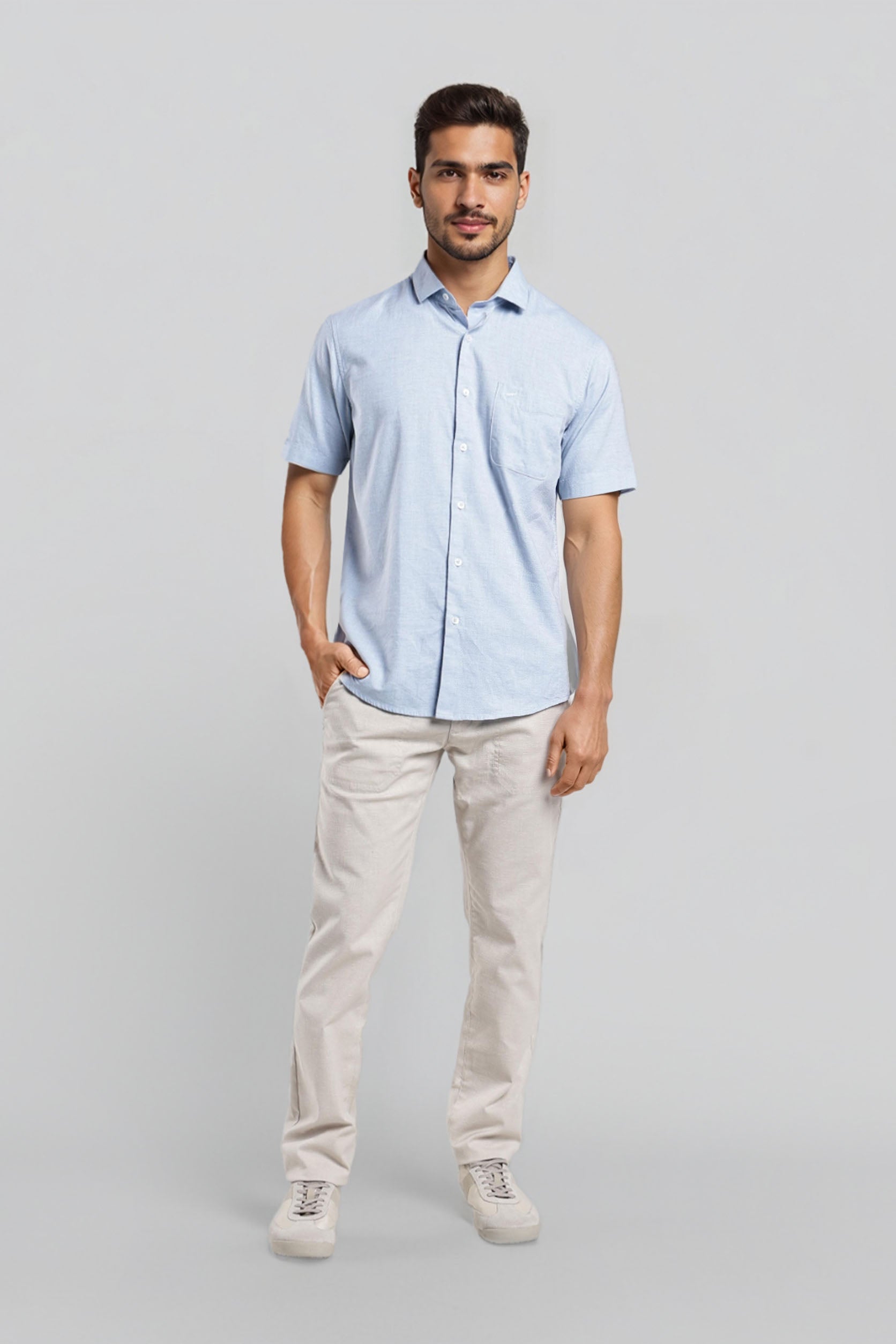 Man wearing a light blue shirt and beige pants on a gray background