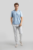 Man wearing a light blue striped polo shirt and white pants on a gray background