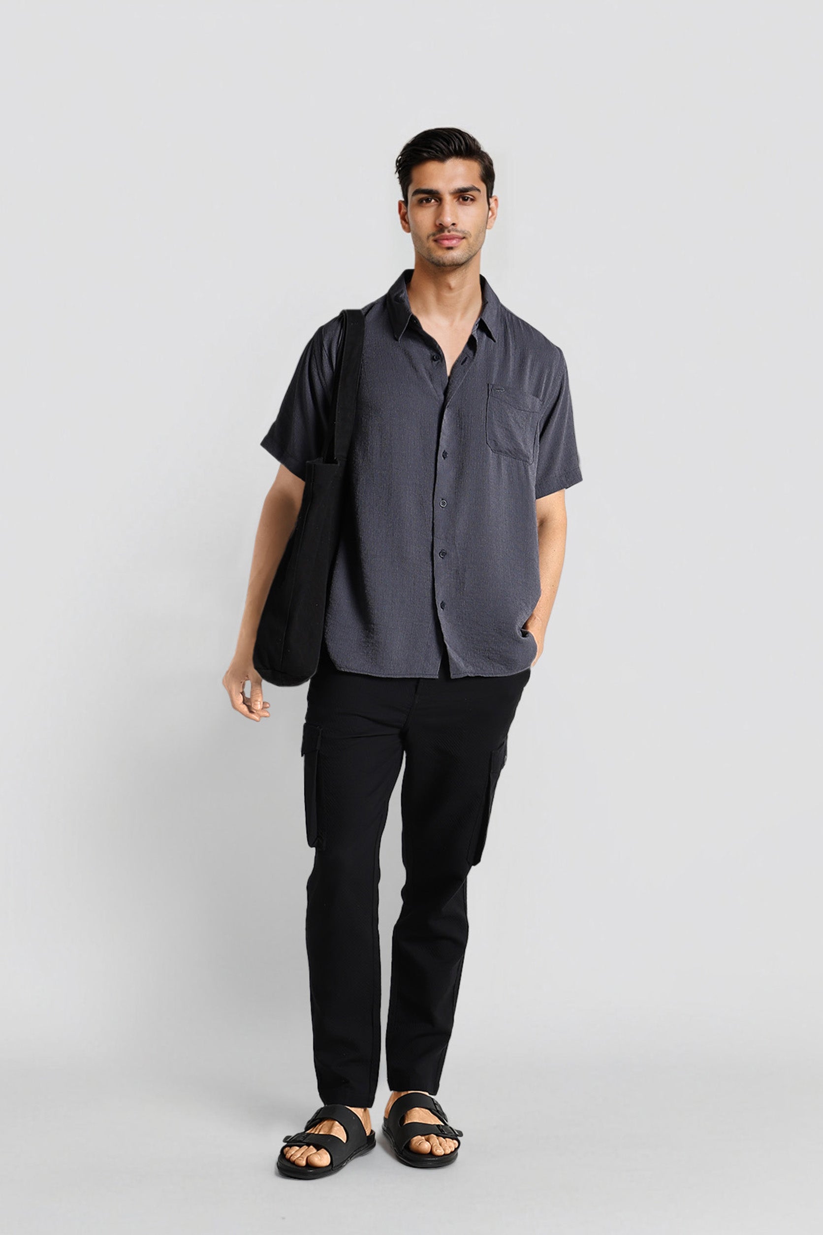 Man wearing a dark gray button-up shirt and black pants on a light gray background