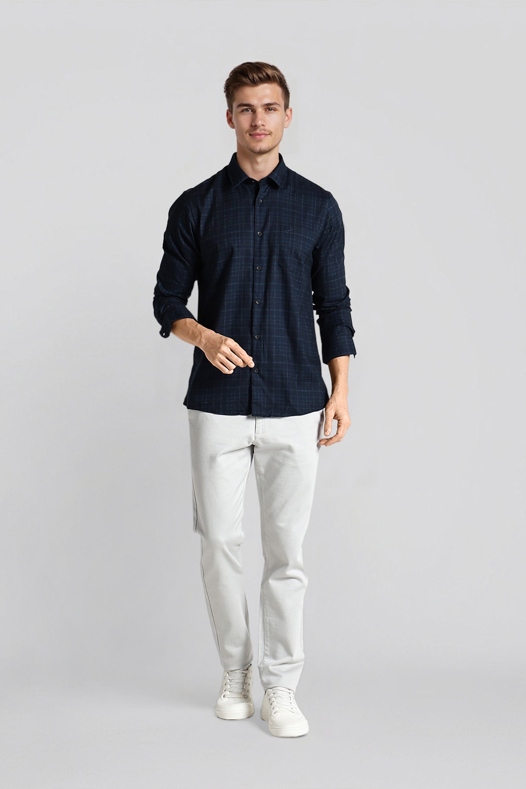 Man wearing a dark blue patterned shirt and white pants on a light gray background