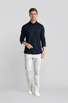 Man wearing a dark blue patterned shirt and white pants on a light gray background