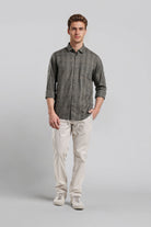 Man wearing a gray button-up shirt and beige pants on a light gray background