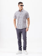 A man wearing a short-sleeve button-up shirt with a gray and white abstract pattern, paired with dark gray trousers, standing against a plain white studio background.