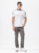 A man modeling a white short-sleeve polo shirt with gray shoulder panels and gray striped trim on the sleeves, paired with gray trousers and black sunglasses, against a plain white background.