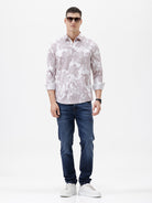 A man wearing a long-sleeve button-up shirt with a light gray and white abstract floral pattern, paired with dark blue jeans, standing against a plain white background.