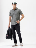 A man wearing a short-sleeve button-up shirt with a gray and white vertical stripe pattern, paired with black pants, standing against a plain white studio background.