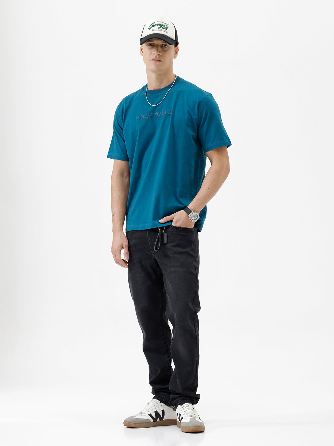 A person wearing slim-fit black jeans, a teal t-shirt, and white sneakers with gray accents, standing against a clean white studio background.