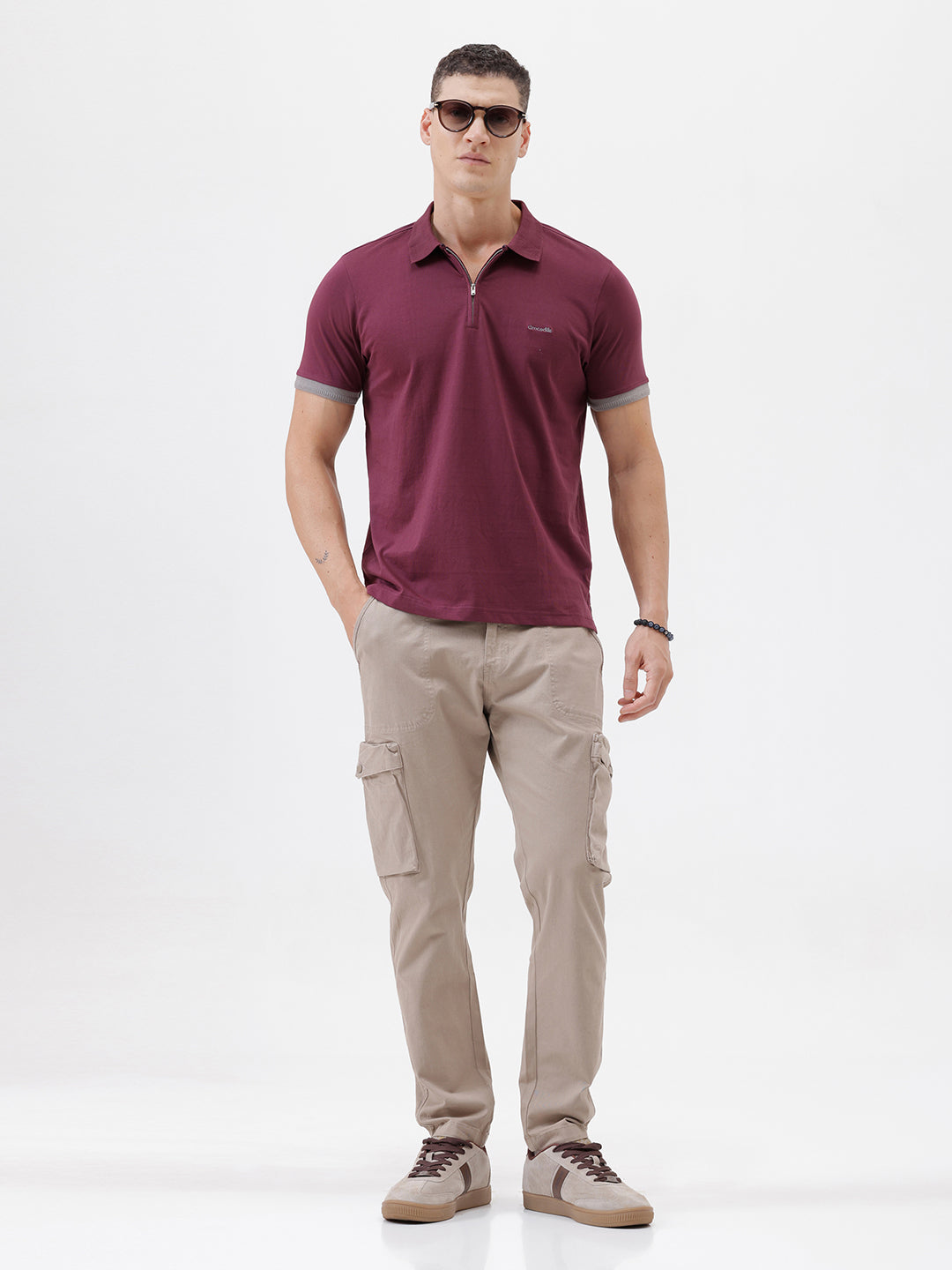 A man wearing a short-sleeve polo shirt in maroon with gray sleeve trim and a half-zip collar, paired with beige cargo pants, against a plain white studio background.