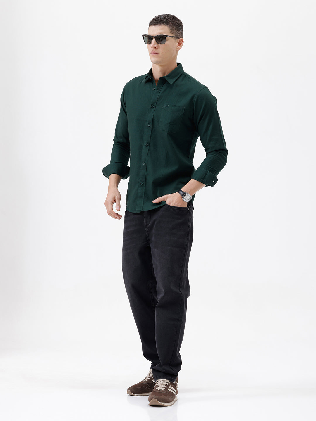 A man wearing a dark forest green long-sleeve button-down shirt with a chest pocket, paired with dark jeans, standing against a plain white studio background.