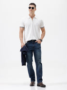 A man wearing a white short-sleeve polo shirt with gray ribbed trim on the collar and sleeve cuffs, paired with dark blue jeans, photographed against a plain white studio background.