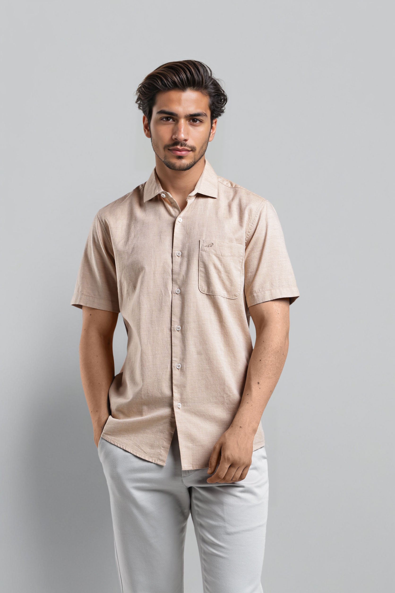 Man wearing a beige shirt and light gray pants against a plain background