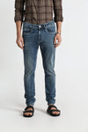 Man wearing a blue blue stone washed mild ripping for a wornout look slim tappered jeans with casual styling on a gray background