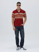 A man wearing a red short-sleeve polo shirt with horizontal cream and rust-orange stripes across the chest and sleeves, paired with dark blue jeans and black sunglasses, against a light gray studio background.