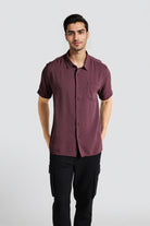 Man wearing a maroon button-up shirt and black pants on a light gray background