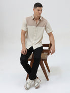 A man wearing a short-sleeve linen button-up shirt with a color-blocked design in beige and cream, paired with black pants, against a plain white studio background.