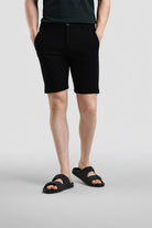 Person wearing black shorts and black sandals on a light gray background