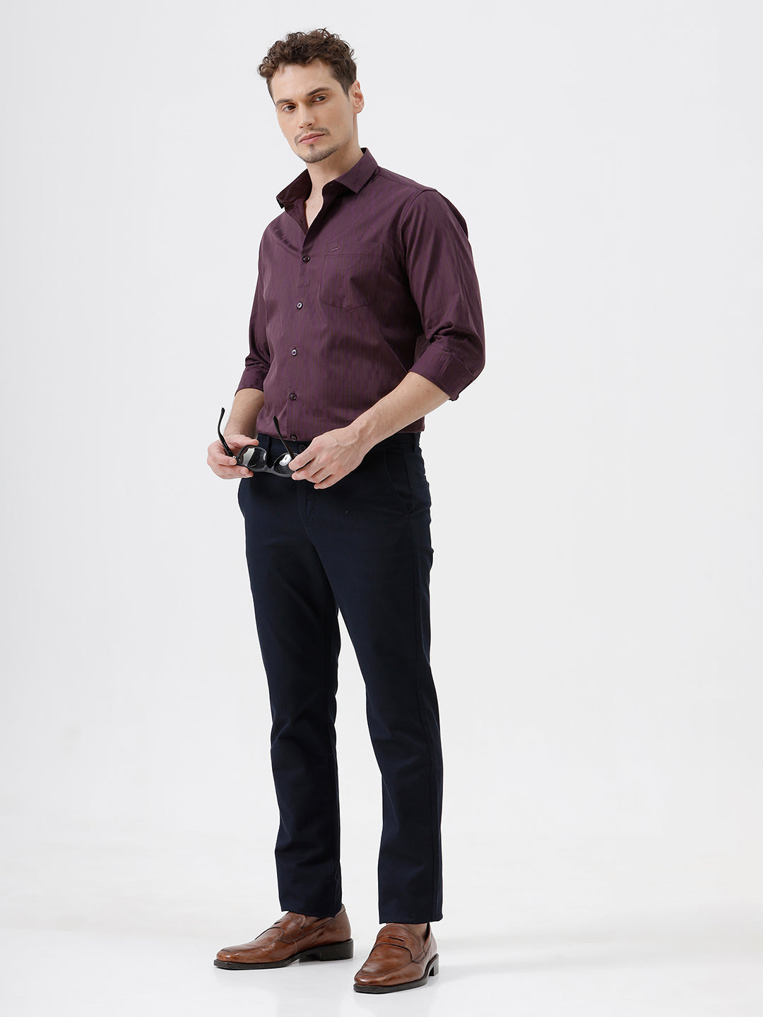 A man wearing a dark purple long-sleeve button-down shirt with subtle vertical stripes and dark navy trousers, standing against a light gray background.