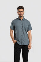 Man wearing a gray button-up shirt and black pants on a light gray background