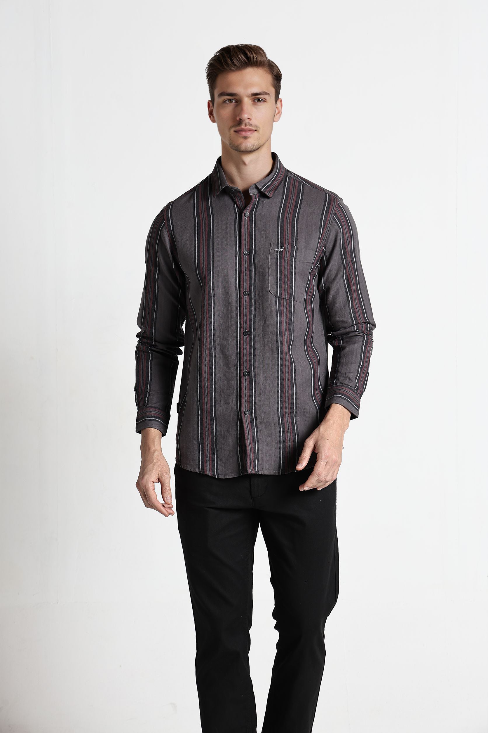 Man wearing a dark patterned shirt and black pants on a white background